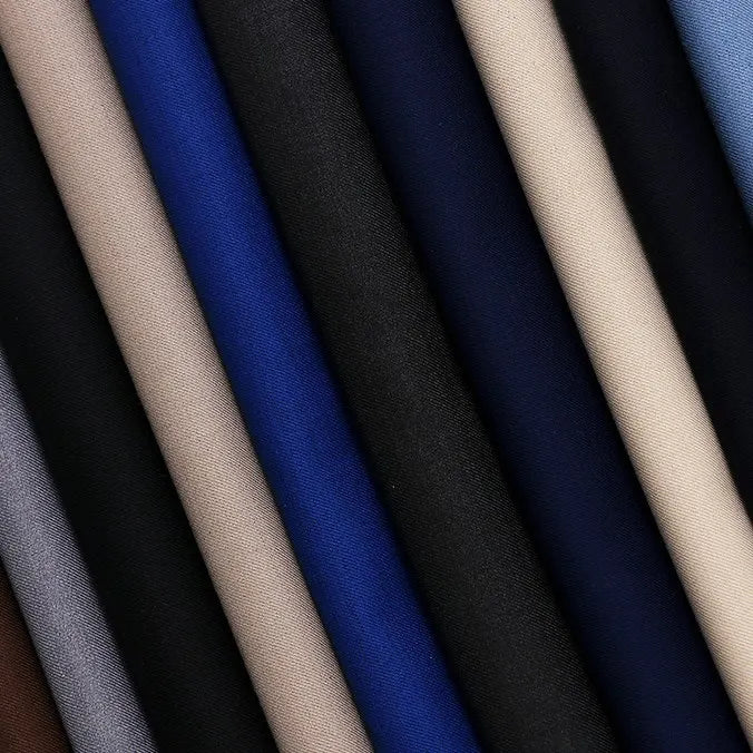 Les rouleaux de Tissu gabardine uni au mètre de Longan Craft France, dans les coloris beige, bleu, noir et gris, sont disposés en diagonale. Fabriqués à partir d'un mélange de laine, de rayonne et de polyester, leur finition lisse et mate les rend parfaits pour les blazers décontractés.