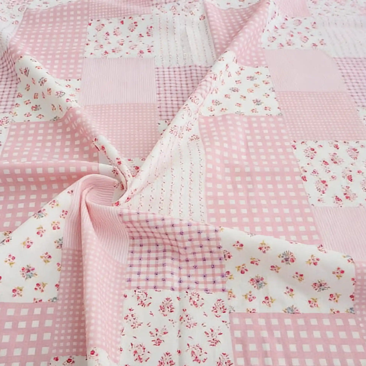 Un patchwork légèrement froissé en popeline de coton au mètre de Longan Craft France, aux motifs floraux et à carreaux pastel, avec une partie froncée formant un tourbillon près du centre.