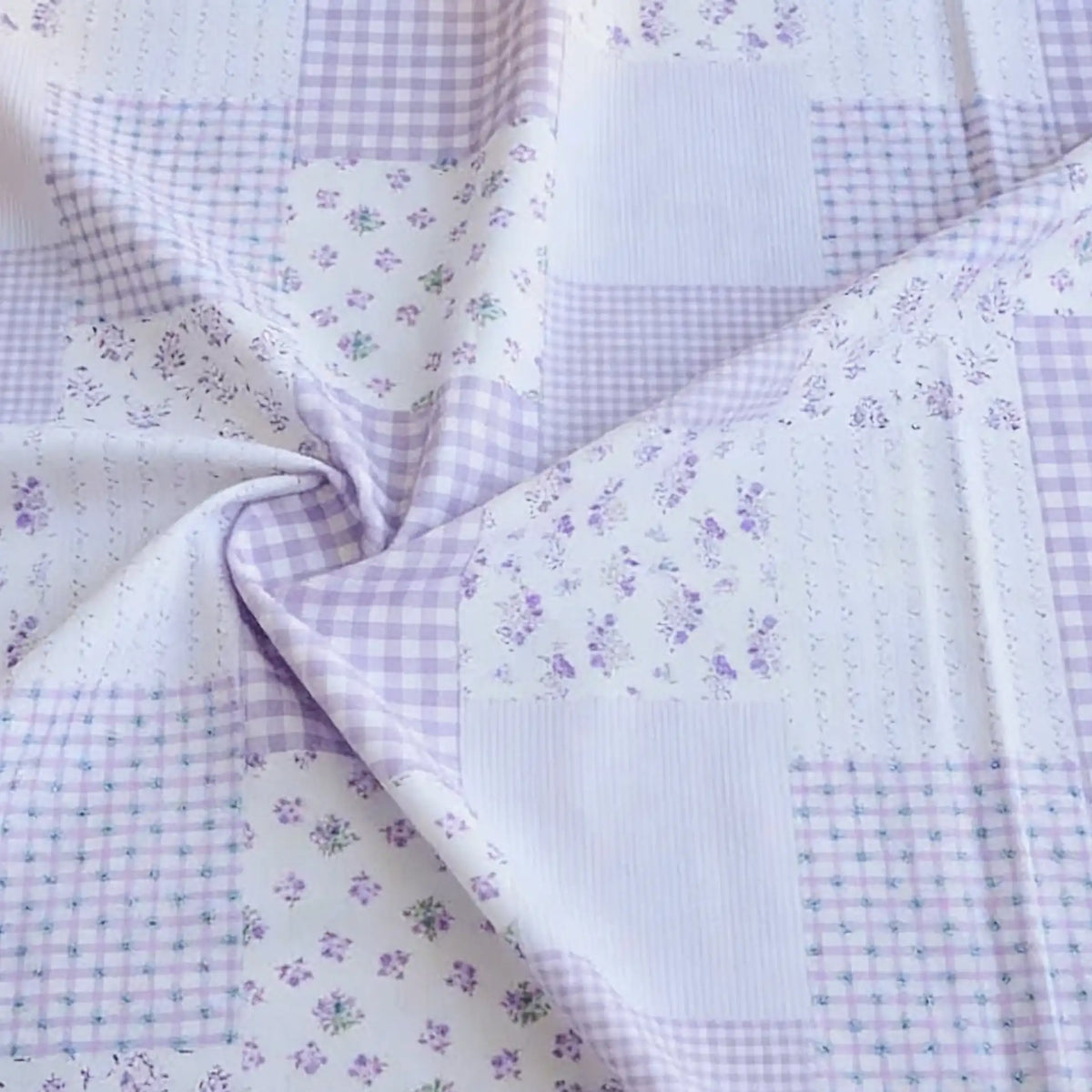 Découvrez le tissu popeline de coton style patchwork au mètre de Longan Craft France : motifs fleurs et carreaux pastel, parfait pour des vêtements stylés. Textile confortable, légèrement froissé, avec motifs variés en nuances violettes et blanches.