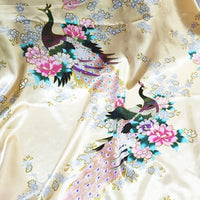 Tissu satin imprimé paon au mètre de Longan Craft France : tissu satiné crème orné de motifs paons colorés, grandes fleurs roses et touches bleues. Idéal pour une décoration intérieure élégante ou des accessoires raffinés.