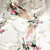 Le Tissu satin imprimé paon au mètre de Longan Craft France est un tissu satin de couleur claire avec des motifs de paons colorés, de fleurs roses, de feuilles vertes et de branches grises, idéal pour créer des accessoires élégants.