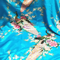 Le Tissu satin imprimé paon au mètre de Longan Craft France présente deux paons colorés parmi des fleurs roses et blanches sur fond bleu brillant, idéal pour accessoires élégants ou créations raffinées.