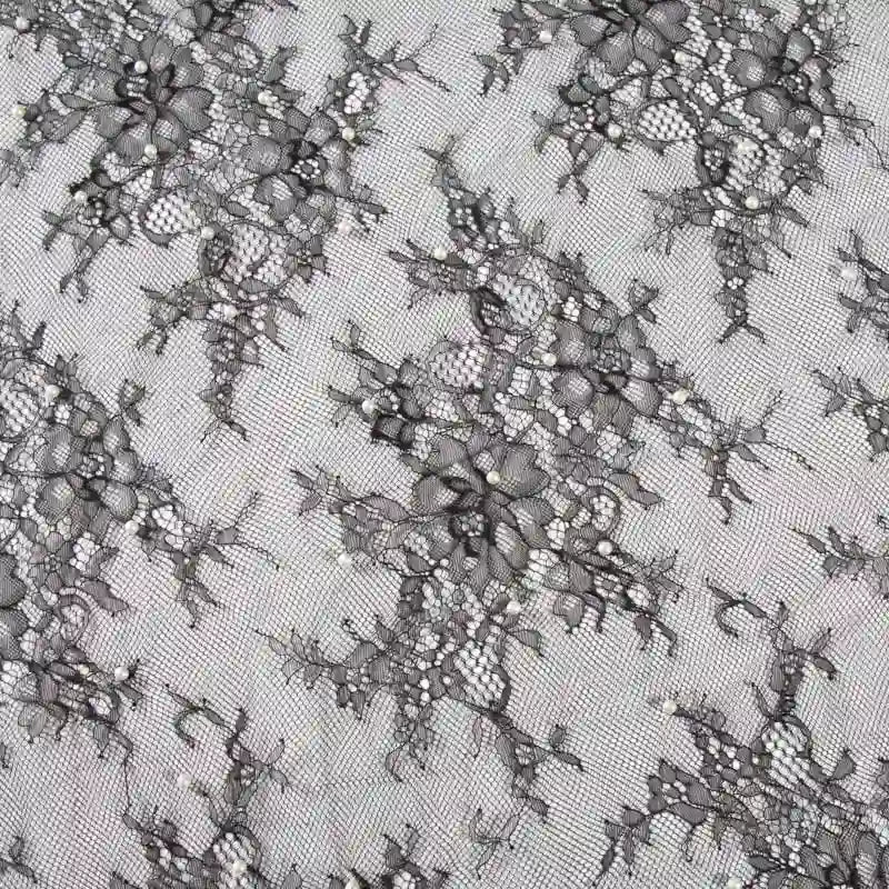 Un gros plan de Dentelle perlée au mètre de Longan Craft France montre des motifs brodés complexes sur une maille transparente - idéal comme tissu dentelle de mariée DIY ou pour des robes de chambre de haute qualité.