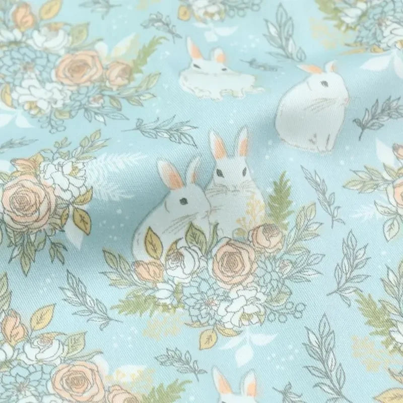 Le Tissu lapin de Pâques rose et bleu au mètre de Longan Craft France est un tissu 100 % coton, orné de lapins blancs et fleurs pastel, idéal pour les projets DIY du printemps ou de Pâques.