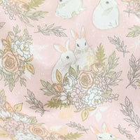 Le tissu lapin de Pâques rose et bleu de Longan Craft France, en 100 % coton, présente des motifs de lapins blancs et fleurs pastel sur fond rose, idéal au mètre pour des projets DIY et déco printaniers.