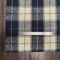 Une règle en métal de 15 cm est posée horizontalement sur un tissu flanelle épaisse brossée à carreaux de Longan Craft France, en polyester-coton, sur une surface en bois foncé.