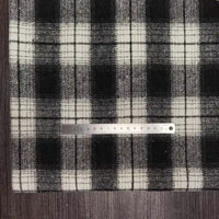 Une règle métallique est posée horizontalement sur le tissu flanelle épaisse brossée un côté à carreaux de Longan Craft France, un plaid confortable en polyester-coton vendu au mètre, présenté sur une surface en bois sombre.