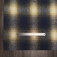 Un morceau de Tissu flanelle épaisse brossée un côté à carreaux au mètre de Longan Craft France à carreaux bleus, jaunes et blancs est posé à plat sur du bois foncé avec une règle métallique de 15 cm placée horizontalement sur le tissu flanelle confortable.