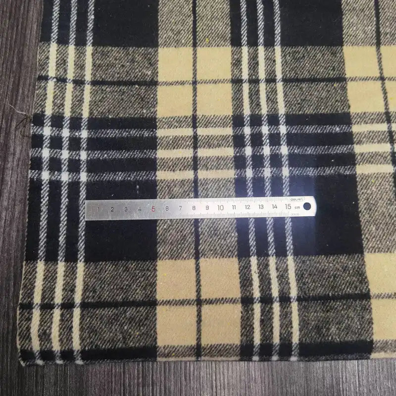 Une règle en métal marquée 0-15 cm repose sur un "Tissu flanelle épaisse brossée un côté à carreaux" jaune et noir de Longan Craft France, un tissu confortable en polyester-coton pour l'automne, posé sur une surface en bois.