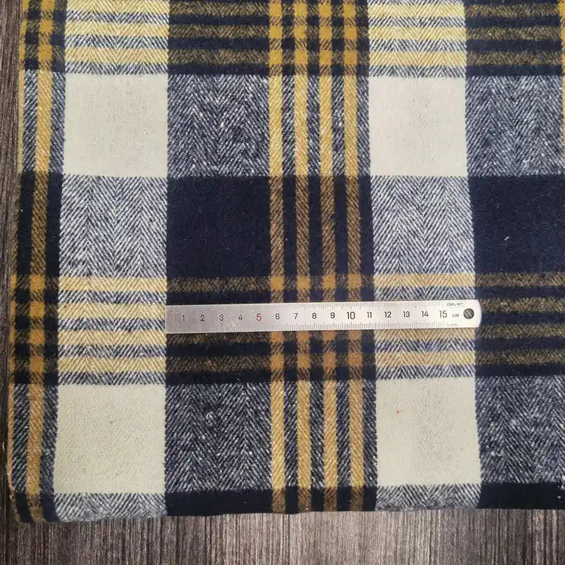 Une règle métallique de 15 cm est posée sur l'épaisse flanelle à carreaux (polyester-coton) de Longan Craft France, à carreaux bleus, blancs et jaunes, reposant sur une surface en bois.