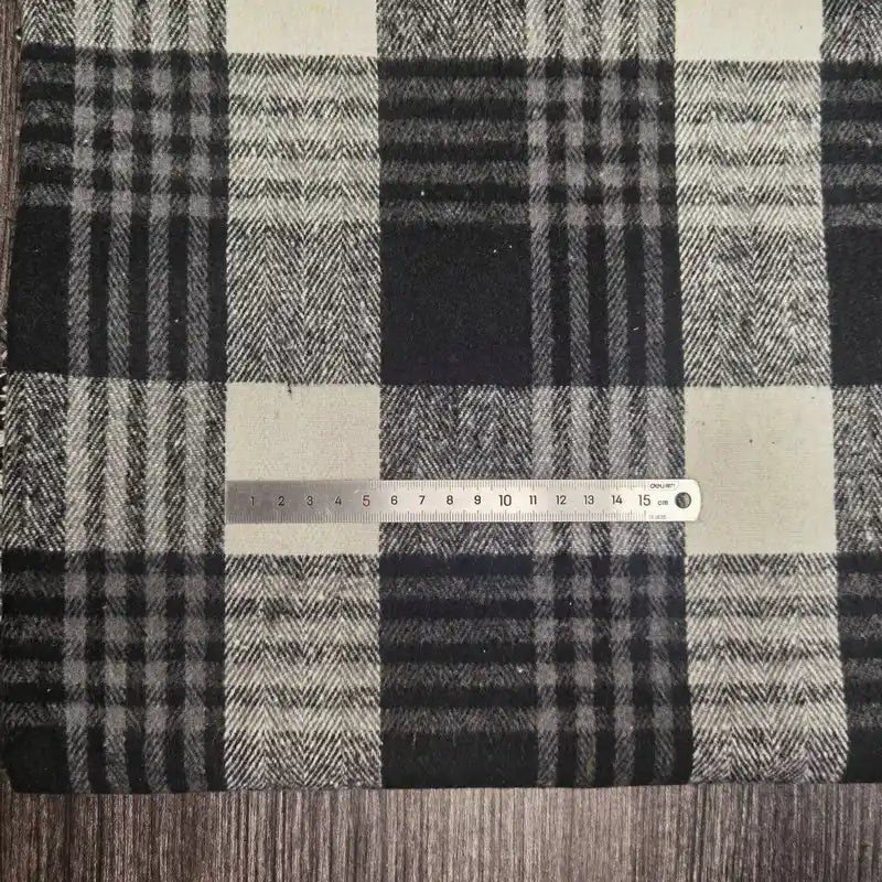 Une règle métallique de 15 cm est placée sur le tissu flanelle épaisse brossée (polyester-coton) de Longan Craft France, qui présente un motif à carreaux noirs, blancs et gris, avec une surface en bois en dessous.