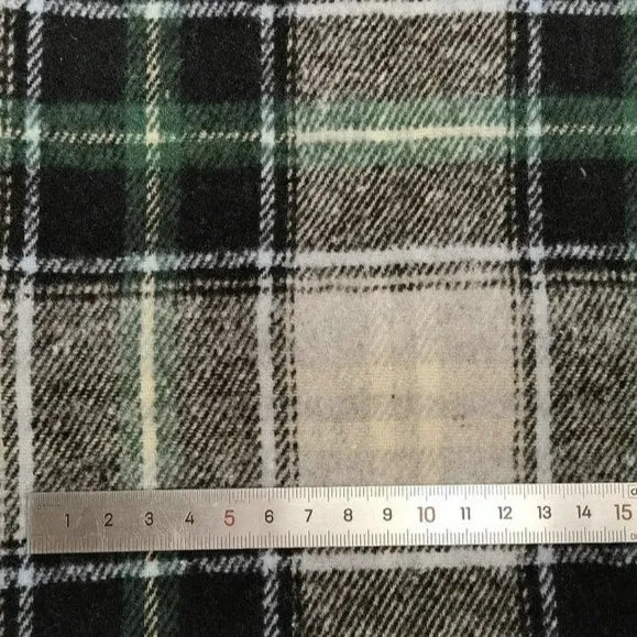 Une règle métallique indique les centimètres au bas d'un tissu écossais vert, noir et blanc Longan Craft France tissu flanelle épaisse brossée un côté - un tissu coloré en polyester-coton vendu au mètre, idéal pour le confort de l'automne.