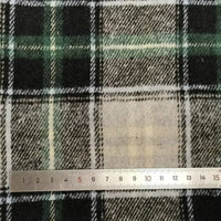 Une règle métallique indique les centimètres au bas d'un tissu écossais vert, noir et blanc Longan Craft France tissu flanelle épaisse brossée un côté - un tissu coloré en polyester-coton vendu au mètre, idéal pour le confort de l'automne.
