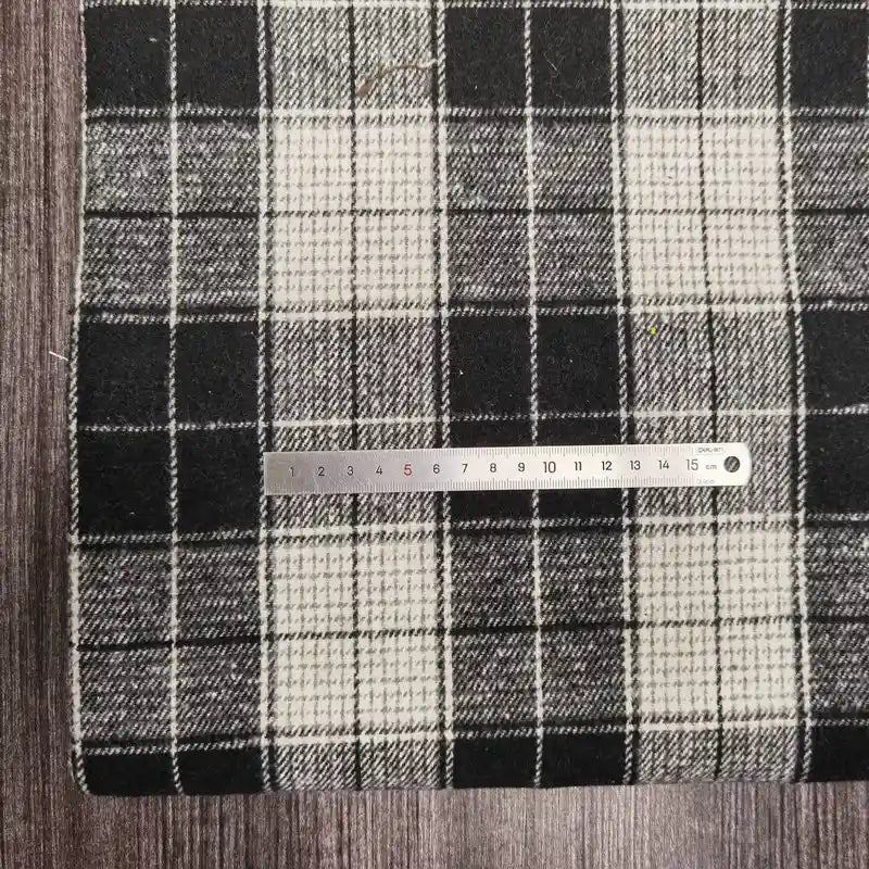Une règle métallique de 1 à 15 cm est posée sur l'épaisse flanelle à carreaux (polyester-coton) de Longan Craft France, parfaite pour l'automne, le tissu reposant sur une surface en bois sombre.