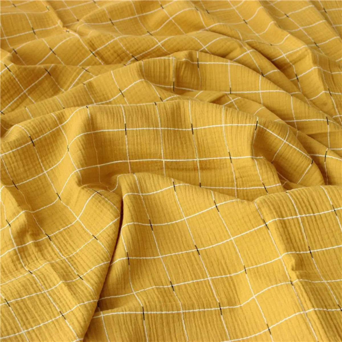 Un gros plan de Tissu double gaze de coton à carreaux au mètre de Longan Craft France montre un tissu jaune doux et texturé avec un motif quadrillé blanc et noir. Ce tissu de coton respirant et confortable est idéal pour divers projets de couture.