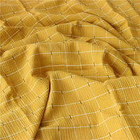 Un gros plan de Tissu double gaze de coton à carreaux au mètre de Longan Craft France montre un tissu jaune doux et texturé avec un motif quadrillé blanc et noir. Ce tissu de coton respirant et confortable est idéal pour divers projets de couture.