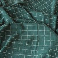 Le "Tissu double gaze de coton à carreaux au mètre" de Longan Craft France est un tissu de coton vert respirant et confortable, avec un toucher texturé, un motif quadrillé blanc et des plis doux pour des créations élégantes.
