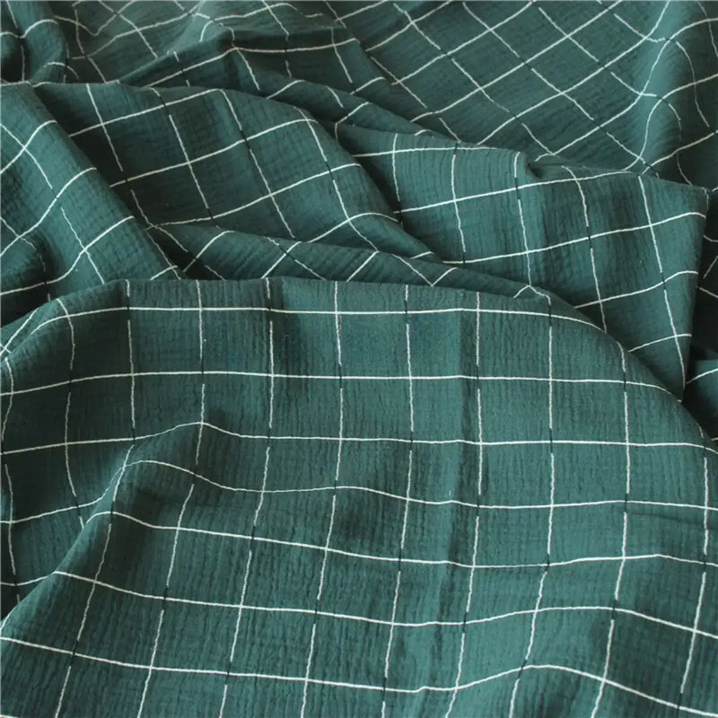Le "Tissu double gaze de coton à carreaux au mètre" de Longan Craft France est un tissu de coton vert respirant et confortable, avec un toucher texturé, un motif quadrillé blanc et des plis doux pour des créations élégantes.