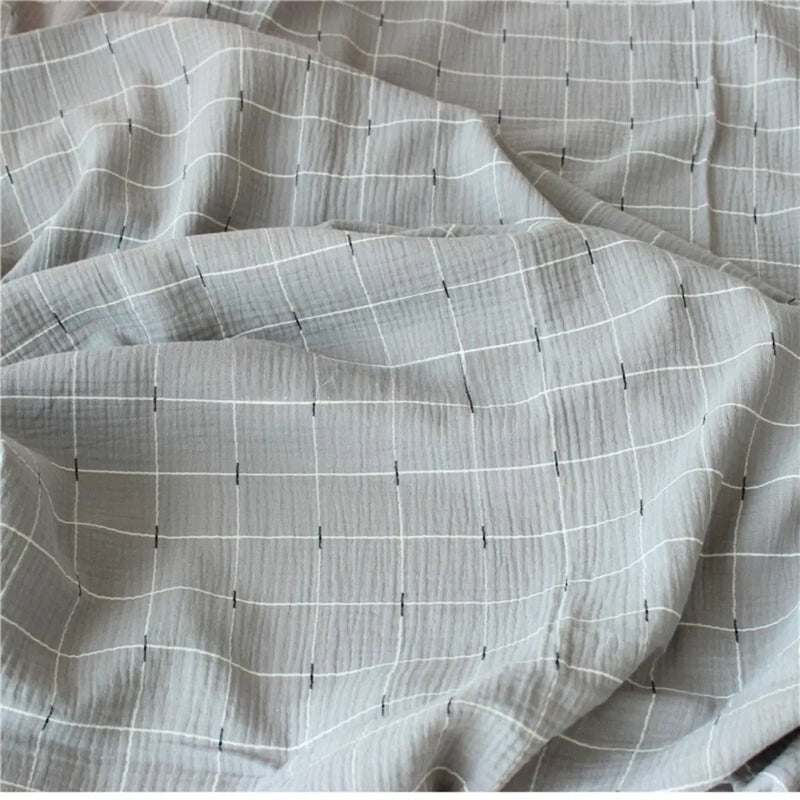 Gros plan sur le tissu double gaze de coton gris clair de Longan Craft France, qui se caractérise par une texture douce et respirante et un motif quadrillé de fines lignes blanches et bleues foncées. Disponible au mètre.