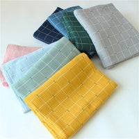 Sept pièces pliées en Tissu double gaze de coton à carreaux au mètre par Longan Craft France, en jaune, bleu clair, vert menthe, rose, bleu marine, vert et gris avec un motif quadrillé blanc, disposées sur une surface blanche.