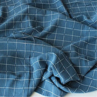 L'image montre le Tissu double gaze de coton à carreaux au mètre de Longan Craft France : un tissu de coton doux et respirant de couleur bleue avec un motif quadrillé blanc, offrant un confort et un design à carreaux classique.