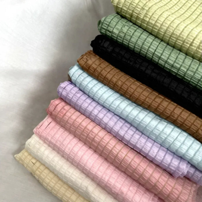 Une pile de tissu lyocell jacquard à carreaux au mètre de Longan Craft France, un textile multicolore respirant idéal pour les vêtements, est soigneusement disposée sur une surface blanche pour une touche d'élégance.