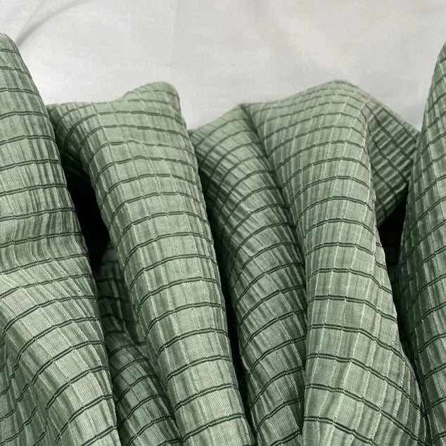 Gros plan sur le tissu lyocell jacquard à carreaux au mètre de Longan Craft France, un textile respirant multicolore pour l'habillement, montrant son subtil quadrillage et ses fines lignes noires disposées en plis souples sur un fond neutre.