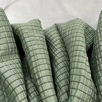 Gros plan sur le tissu lyocell jacquard à carreaux au mètre de Longan Craft France, un textile respirant multicolore pour l'habillement, montrant son subtil quadrillage et ses fines lignes noires disposées en plis souples sur un fond neutre.