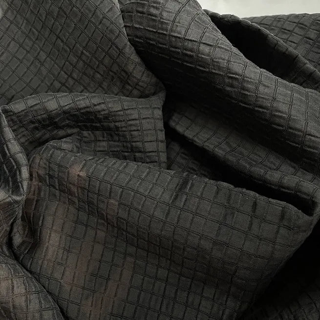 Un gros plan du tissu lyocell jacquard à carreaux au mètre de Longan Craft France montre les plis et les froissures, mettant en valeur le quadrillage multicolore en relief et la texture fine de ce textile respirant pour vêtements.