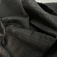 Un gros plan du tissu lyocell jacquard à carreaux au mètre de Longan Craft France montre les plis et les froissures, mettant en valeur le quadrillage multicolore en relief et la texture fine de ce textile respirant pour vêtements.