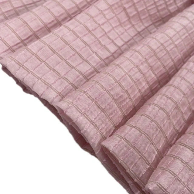 Gros plan sur le tissu lyocell jacquard à carreaux au mètre de Longan Craft France : rose pâle, respirant, avec un quadrillage de fines lignes beiges. Le textile multicolore présente une surface texturée et des plis doux et réguliers, idéaux pour les projets de vêtements.