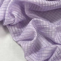 Gros plan sur le jacquard Tissu lyocell à carreaux au mètre de Longan Craft France, de couleur violet clair avec un motif quadrillé. Ce textile léger, respirant et semi-transparent est parfait pour les vêtements élégants.