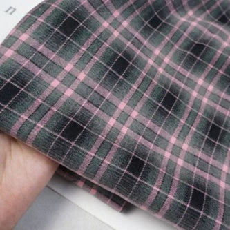 Gros plan d'une main tenant Longan Craft France tissu flanelle mammouth à carreaux vintage au mètre, présentant un motif écossais rose et vert foncé qui met en valeur le tissage polyester-rayonne confortable, idéal pour les chemises.
