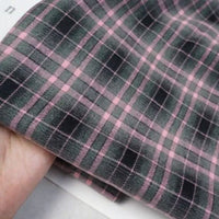 Gros plan d'une main tenant Longan Craft France tissu flanelle mammouth à carreaux vintage au mètre, présentant un motif écossais rose et vert foncé qui met en valeur le tissage polyester-rayonne confortable, idéal pour les chemises.
