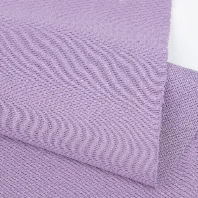 Gros plan sur un pli violet clair de Longan Craft France Tissu French terry uni au mètre, un tissu d'hiver doux en polyester avec une surface légèrement texturée et des bords nets, présenté sur un fond blanc.