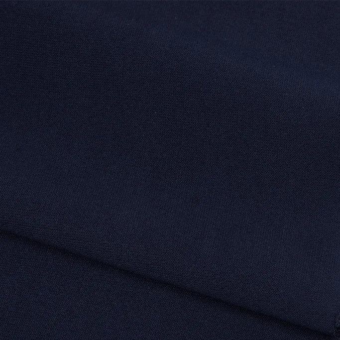 Gros plan sur le pliage de Longan Craft France Tissu French terry uni au mètre - polyester bleu marine foncé à la texture lisse et mate et au tissage fin. Ce tissu doux est idéal pour les vêtements d'hiver et est bien rangé sur l'image.