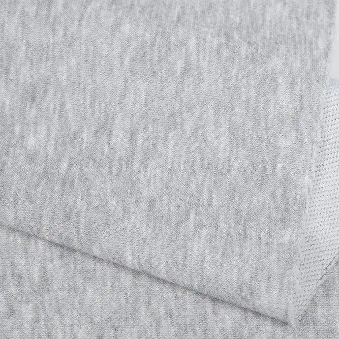 Un gros plan du Tissu French terry uni au mètre de Longan Craft France montre deux pièces gris clair qui se chevauchent, avec une surface lisse et subtilement texturée et un bord légèrement plié - un tissu polyester doux parfait pour les vêtements d'hiver.