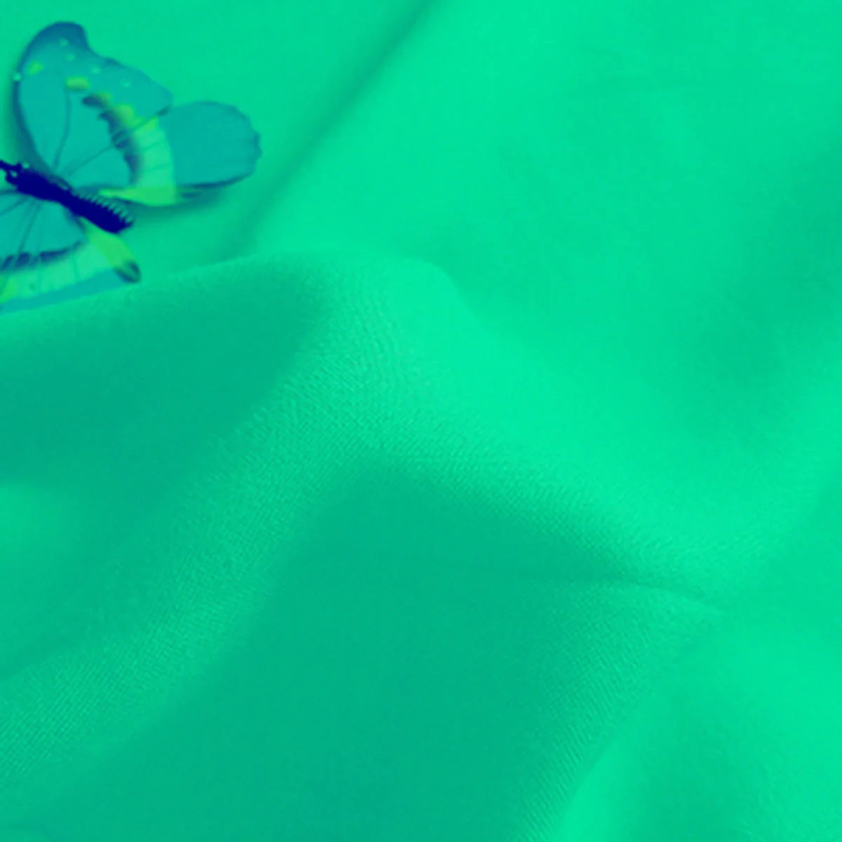 Un pli visible apparaît sur le Tissu jersey viscose uni au mètre de Longan Craft France, avec un papillon bleu en haut à gauche. Le filtre verdâtre met en évidence la douceur de la viscose 100% rayonne, idéale pour la confection de robes.