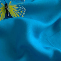Un papillon bleu et jaune se pose sur le Tissu jersey viscose uni au mètre - 100 % viscose rayonne - bleu vif de Longan Craft France, idéal pour les robes, avec des plis et des ombres visibles.