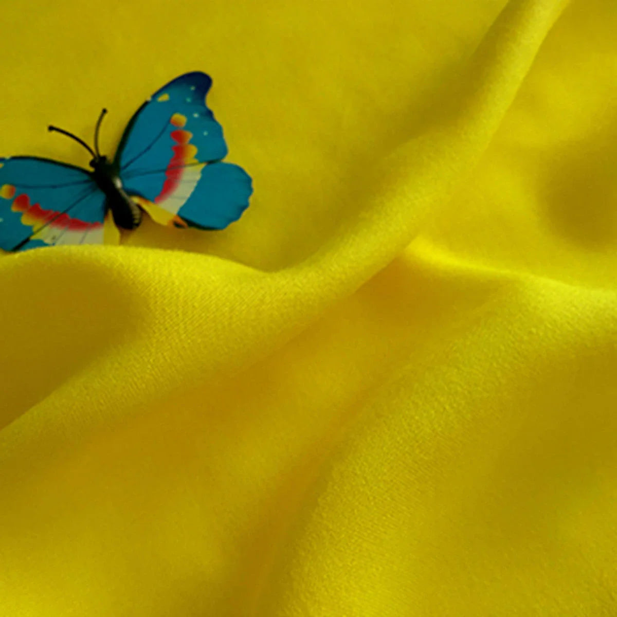 Un papillon bleu avec des marques orange et jaunes repose sur le Tissu jersey viscose uni au mètre de Longan Craft France, 100% viscose rayonne - idéal pour les peignoirs grâce à sa texture lisse et élégante et à son drapé.