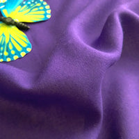 Gros plan sur l'uni de viscose Tissu jersey (100 % rayonne) de Longan Craft France, lisse et violet, avec des plis doux et un détail de papillon jaune-bleu dans le coin supérieur gauche, idéal pour les robes.