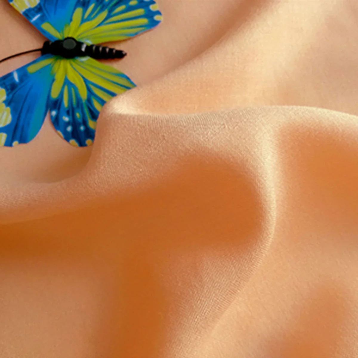 Un papillon bleu et jaune est posé sur un Tissu jersey viscose uni au mètre de Longan Craft France, un tissu 100% rayonne idéal pour les robes, avec des plis visibles et une texture douce.