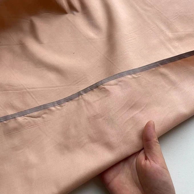 Une main tient un morceau de Taffetas de soie uni au mètre de Longan Craft France, 100 % soie de mûrier en pêche claire avec une couture visible et une bande transparente cousue le long du bord - idéal pour les robes de mariée.
