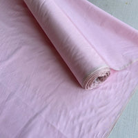 Un rouleau de Taffetas de soie uni au mètre de Longan Craft France, fabriqué à partir de 100% de soie de mûrier rigide, partiellement déroulé pour révéler sa texture lisse et légèrement translucide, idéale pour les robes de mariée de haute qualité.