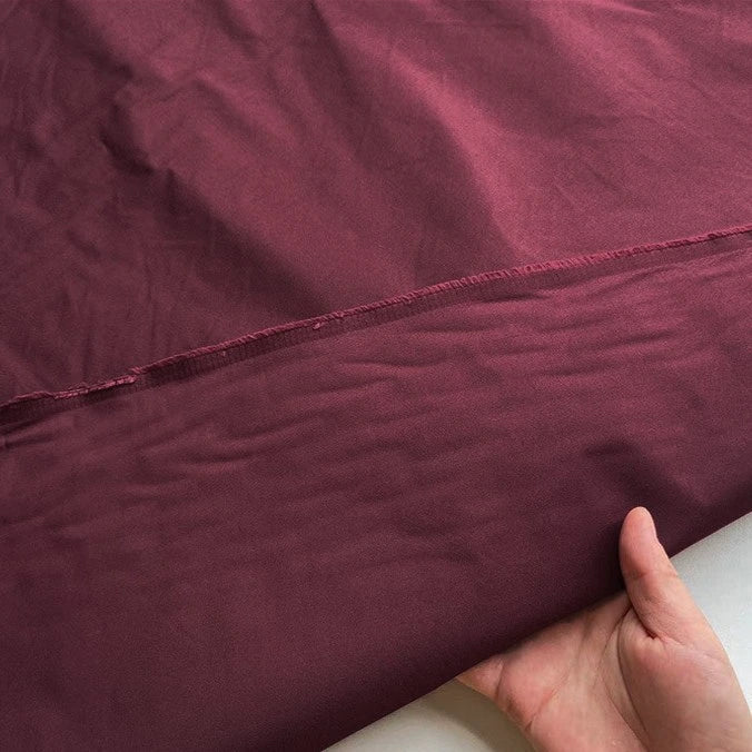 Une personne tient un morceau de "Taffetas de soie uni au mètre" marron de Longan Craft France, fabriqué à 100 % en soie de mûrier, un tissu rigide de haute qualité idéal pour les robes de mariée. Une couture visible traverse le milieu sur un fond blanc.