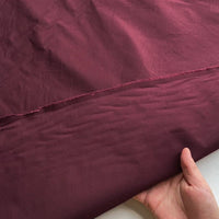 Une personne tient un morceau de "Taffetas de soie uni au mètre" marron de Longan Craft France, fabriqué à 100 % en soie de mûrier, un tissu rigide de haute qualité idéal pour les robes de mariée. Une couture visible traverse le milieu sur un fond blanc.
