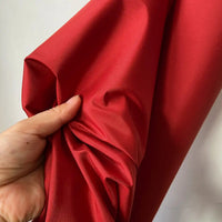 Une main tient et froisse légèrement un morceau de Taffetas de soie uni au mètre de Longan Craft France - tissu de soie de mûrier rigide à 100 %, idéal pour les robes de mariée - sur un fond uni et clair.