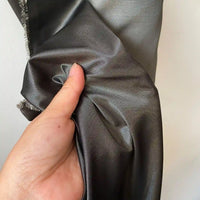 Une main présente un morceau de Taffetas de soie uni au mètre de Longan Craft France, un tissu 100% soie de mûrier gris foncé et brillant, à la texture lisse et réfléchissante, idéal pour les robes de mariée de haute qualité.
