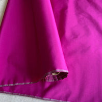 Un rouleau de Taffetas de soie uni au mètre de Longan Craft France, fabriqué à partir de 100 % de soie de mûrier, est partiellement déroulé pour révéler sa texture lisse, idéale pour les robes de mariée de qualité.