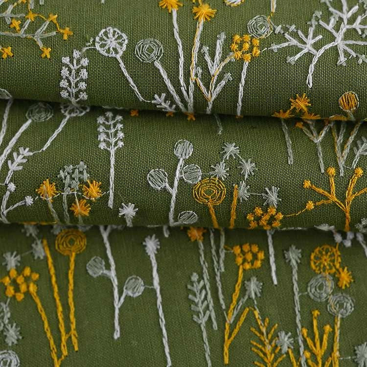 Le Tissu brodé de motifs végétaux au mètre de Longan Craft France, vert avec des motifs blancs et jaunes, est idéal pour vêtements, accessoires ou décoration grâce à ses délicates fleurs et tiges répétées.